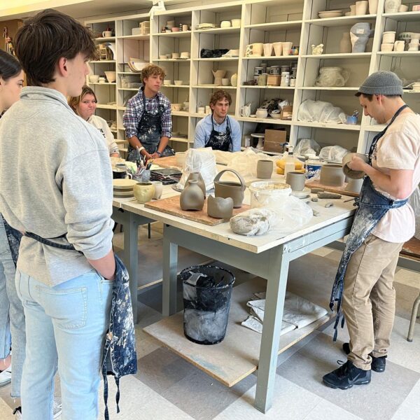 student works on ceramics piece as students observe