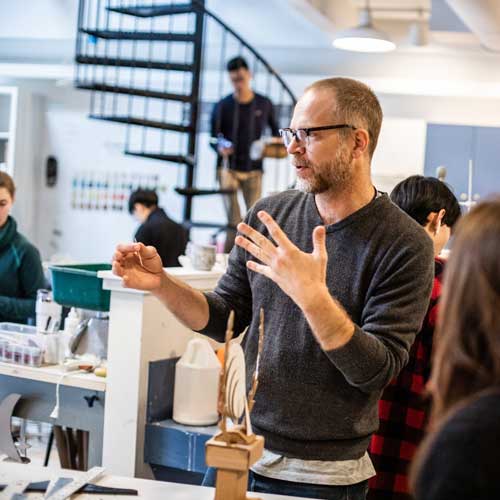 man with glasses gesticulating in art room with students